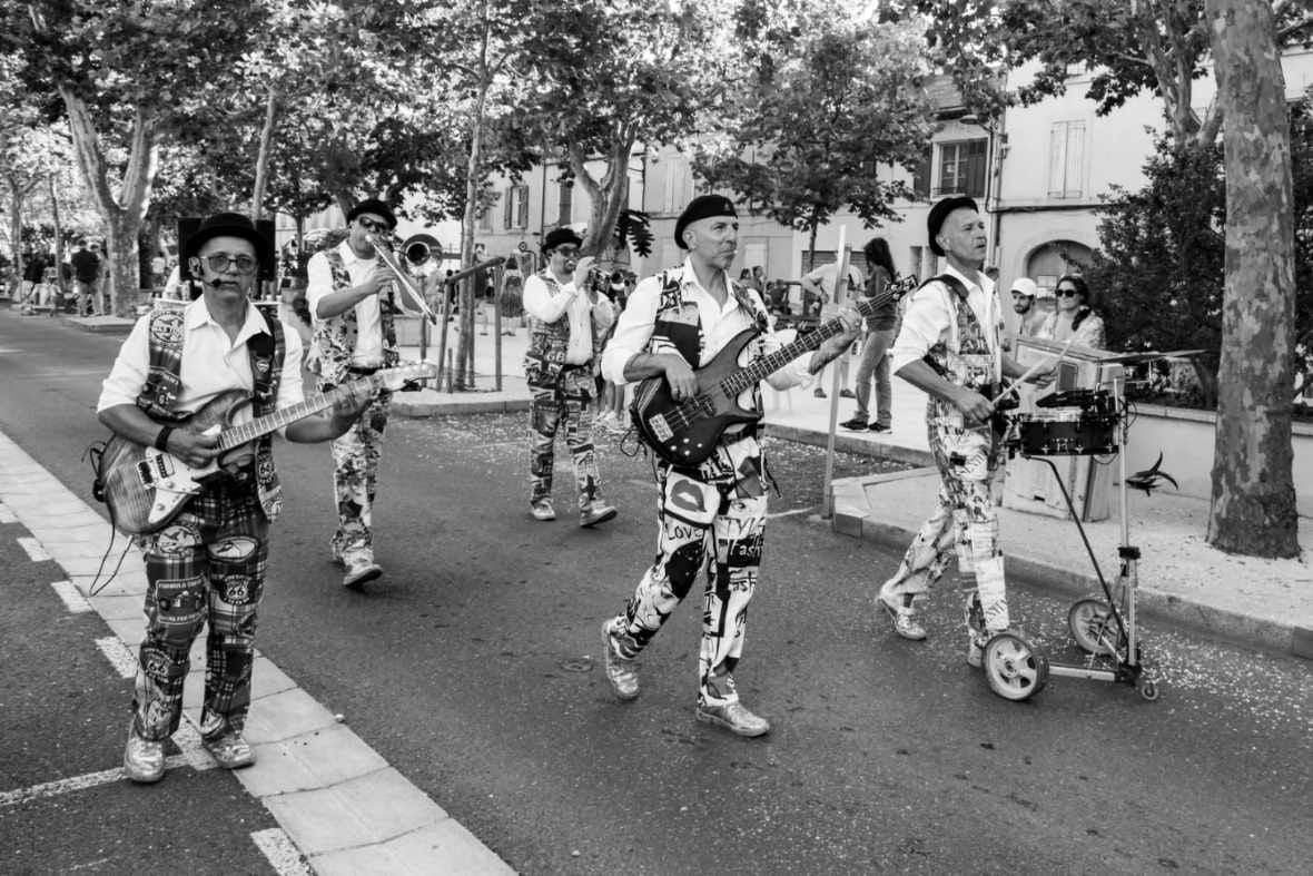 Le groupe joue en marchant dans une rue bordée de platanes, photo noir et blanc