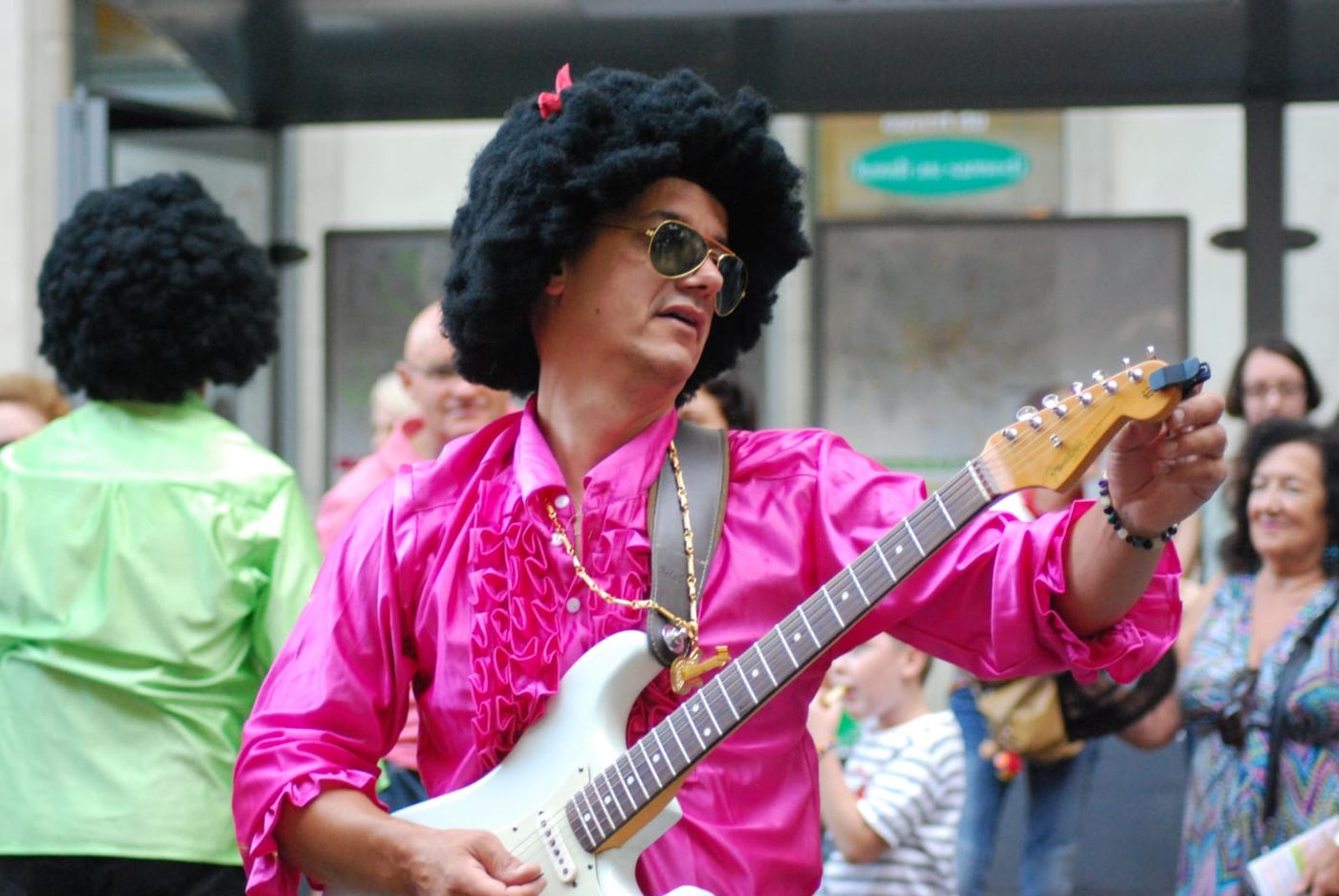 Michel à la guitare en perruque afro et chemise rose, déguisé pour une soirée disco