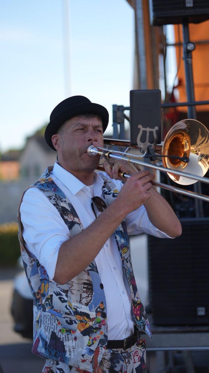 Pascal joue du trombone sur scène, chapeau melon et gilet imprimé